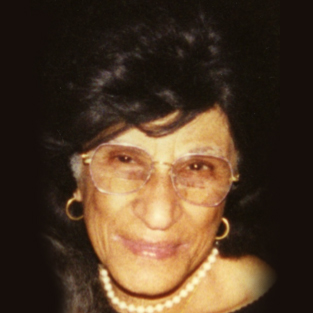Photograph of Valentina Almeida -- headshot of a woman wearing glasses, small gold hoops, and a pearl necklace.