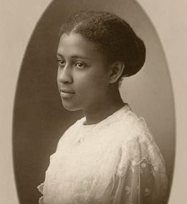 Photograph Of Rosamond A. Guinn - A Woman With Her Dark Hair Tied Back In A Bun, Wearing A Flowy White Dress