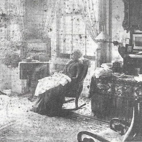 Photograph of Cornelia Grinnell - older woman in a dark dress sitting in a rocking chair inside a home, possibly a living room.