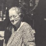 Photograph Of Mary Ann Hayden - An Older Woman With Short Grey Hair And Round Glasses, She Is Wearing A Floral Print Dress