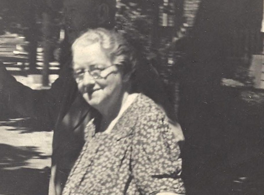 Photograph Of Mary Ann Hayden - An Older Woman With Short Grey Hair And Round Glasses, She Is Wearing A Floral Print Dress