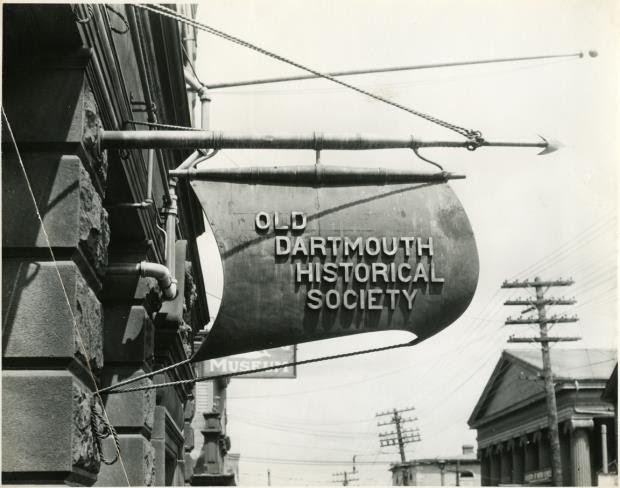 A sign that reads “Old Dartmouth Historical Society” mounted on the side of a stone building.