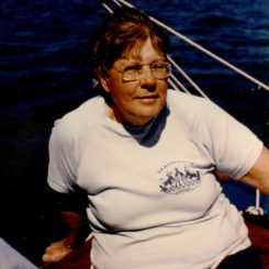 Photograph Of Louise Strongman - She Is Sitting On A Boat With Short Red Hair, Glasses, White Shirt And Shorts