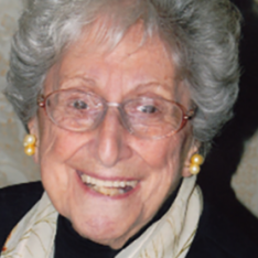 Photograph Of Loretta Bourque - A Headshot Of An Older Woman With Round Glasses And Short Grey Hair. She Is Smiling At The Camera