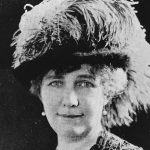 Photograph Of Alice Howland Macomber - Bust Of Woman With Short Light Hair Wearing Pearl Earrings, A Black Lacy Top, And A Large Feathered Hat.