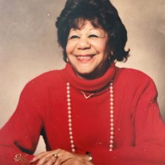 Photograph Of Zoe Alysse Washington Fabio - A Woman With Medium Length Black Hair, She Is Wearing A Red Sweater And A Pearl Necklace