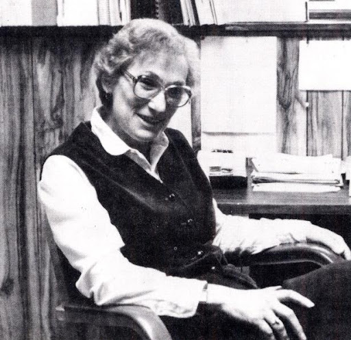 A Photograph Of Rubye Finger- A Black And White Mid Shot Of A Woman With Thick Cirular Rimmed Glasses And A Sweater Vest Sitting And Looking To The Camera