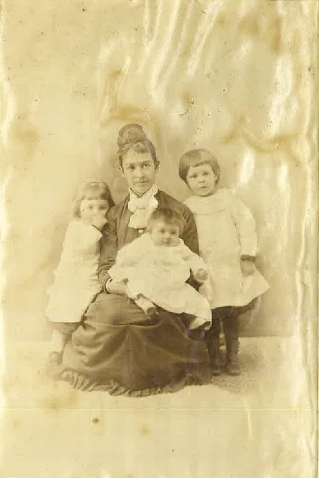 A photograph of Frances Eliot Gifford. A time-weathered image of a woman sitting with her three children.